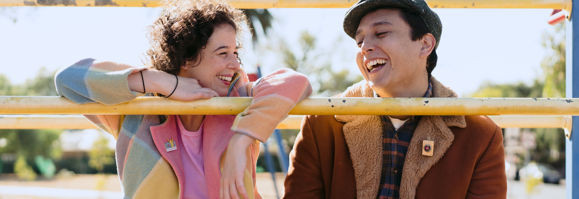 A couple laughing while sitting on a yellow fence railing 